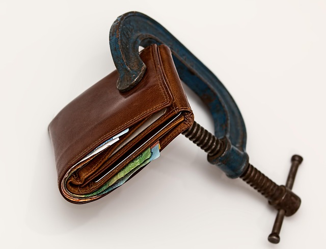 A photo of a wallet with cash being sqeezed by a metal clamp.